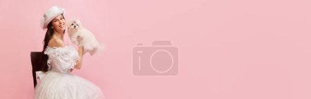 Téléchargez les photos : Portrait of beautiful lady, woman in white vintage dress posing with lovely cute dog over pink background. Banner. Concept of 19th century, fashion, comparison of eras, history, retro style - en image libre de droit