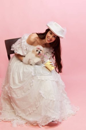 Photo for Coffee. Portrait of beautiful lady in white vintage dress posing with cute little dog over pink background. Concept of 19th century, fashion, comparison of eras, history, retro style - Royalty Free Image