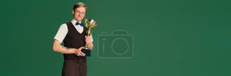 Photo for Winning trophy. Success. Portrait of man in stylish classical clothes, shorts and vest posing over green studio background. Concept of emotions, facial expression, lifestyle, retro fashion. Ad - Royalty Free Image
