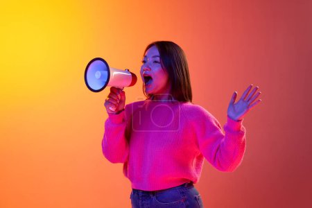 Téléchargez les photos : News, information. Young girl in pink sweater talking in megaphone over gradient orange background in neon light. Concept of emotions, facial expression, youth, lifestyle, inspiration, sales, ad - en image libre de droit