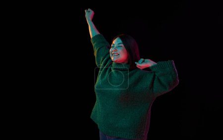 Photo for Excitement. Cheerful mood. Young emotional brunette girl in cozy sweater posing over dark background in neon light. Concept of emotions, facial expression, youth, inspiration, sales, ad - Royalty Free Image
