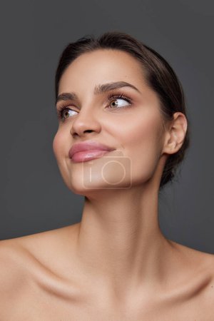 Foto de Anti-wrinkles care. Eco products. Beautiful brunette young girl with smooth well-kept skin posing over grey background. Concept of natural beauty, skin care, cosmetology, cosmetics, health, fashion - Imagen libre de derechos