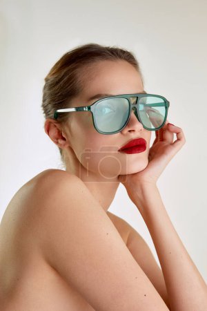 Foto de Modern fashion look, attraction. Young beautiful girl with red lips posing in green sunglases over grey studio background. Concept of natural beauty, skin care, cosmetology, cosmetics, health, fashion - Imagen libre de derechos