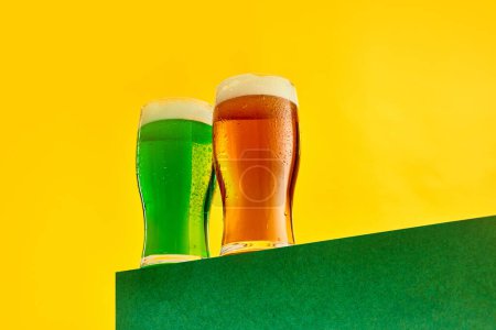 Foto de Two glasses of chill green and lager foamy beer over yellow background. Celebration, festival. Concept of st patricks day celebration, brewery, traditions, alcohol drinks, taste, Irish holiday - Imagen libre de derechos