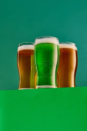Photo for Three glasses with green and lager foamy beer over green background. Traditional hop taste. Concept of st patricks day celebration, brewery, traditions, alcohol drinks, taste, Irish holiday - Royalty Free Image