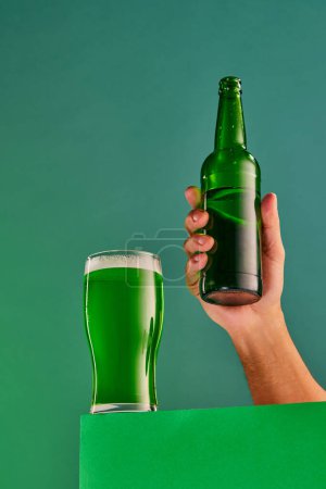Foto de Popular and favorite drink. Glass and bottle of green foamy beer over green background. Concept of st patricks day celebration, brewery, traditions, alcohol drinks, taste, Irish holiday - Imagen libre de derechos