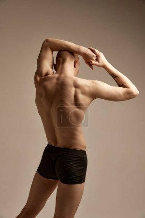 Téléchargez les photos : Rear view portrait of muscular male body, relief back over grey studio background. Young model posing in underwear. Concept of mens health and beauty, body and skin care, fitness. Body art - en image libre de droit