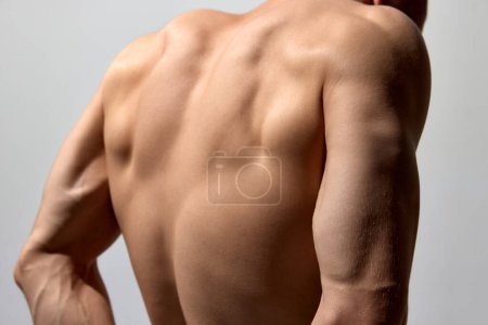 Téléchargez les photos : Cropped photo of relief, strong, muscular back and hands. Male model posing shirtless isolated over light grey background. Concept of mens health and beauty, body and skin care, fitness. Body art - en image libre de droit