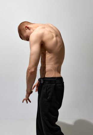 Téléchargez les photos : Round back. Masculinity aesthetics. Young man posing shirtless over light grey background. Muscular body shape. Concept of mens health and beauty, body and skin care, fitness. Body art - en image libre de droit