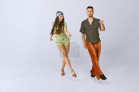 Foto de Step by step. Young talented disco dancers, man and woman, in stylish retro clothes dancing, performing isolated over grey studio background. 70s fashion, hobby, creativity, hippie, American culture - Imagen libre de derechos
