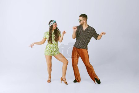 Téléchargez les photos : Le bonheur. Jeune homme et femme élégants dans des tenues rétro danse émotionnellement disco danse isolé sur fond de studio gris. mode des années 70, hobby, créativité, mode de vie hippie, culture américaine - en image libre de droit