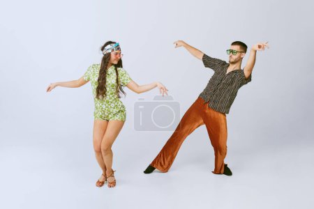 Téléchargez les photos : Pretty young girl and handsome man in stylish retro clothes dancing disco dance isolated over grey studio background. 70s fashion, hobby, creativity, hippie lifestyle, American culture - en image libre de droit