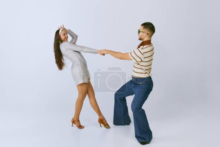 Téléchargez les photos : Spinning. Young beautiful girl in silver dress and stylish man dancing disco dance isolated over grey studio background. 70s fashion, hobby, creativity, hippie lifestyle, American culture - en image libre de droit