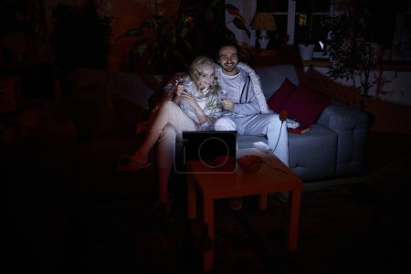 Photo for Power bank lamp light. Young man and woman sitting together on couch at home in the evening and watching movie on laptop. No electricity, blackout. Concept of power outage, relationship - Royalty Free Image