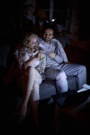 Photo for Cheers. Romantic date night. Young man and woman sitting together on couch at home in the evening and drinking wine. No electricity, blackout. Concept of power outage, relationship - Royalty Free Image