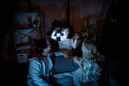 Game in dark room. Family gathering in living room. Man, woman and girl, child playing together at home in the evening. No electricity, blackout. Concept of power outage, relationship, childhood