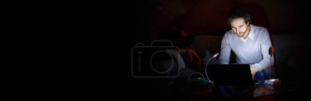 Photo for Unstable electricity. Man, freelancer sitting on sofa at home in evening, working on laptop with battery lamp light. Blackout, no electricity. Concept of power outage. Banner. Copy space for ad, text - Royalty Free Image