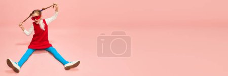 Foto de Linda niña, niño con dos coletas posando en vestido rojo y medias azules sobre fondo de estudio rosa. Concepto de infancia, emociones, moda, expresión facial. Banner. Copiar espacio para anuncios, texto - Imagen libre de derechos