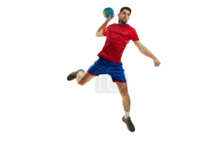Téléchargez les photos : Jeter une balle dans un saut. Jeune homme, joueur de handball professionnel en uniforme rouge, s'entraînant isolé sur fond de studio blanc. Sport, action, mouvement, championnat, style de vie sportif concept - en image libre de droit