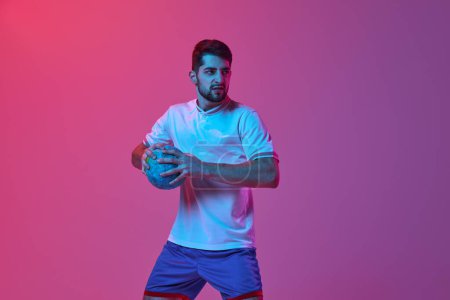 Photo for Ready to win. Young man, professional handball player posing isolated over gradient pink background in neon light. Concept of sport, action, motion, championship, sportive lifestyle - Royalty Free Image