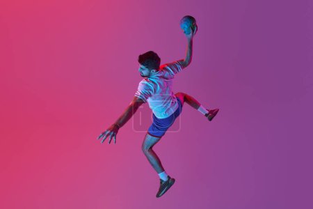 Foto de Top view. In a jump. Young man, professional handball player training, playing isolated over gradient pink background in neon light. Winner. Concept of sport, action, championship, sportive lifestyle - Imagen libre de derechos