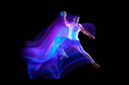 Téléchargez les photos : Throwing ball in a jump. Young man, professional handball player in motion, playing over black background with mixed lights effect. Concept of sport, action, motion, championship, sportive lifestyle - en image libre de droit