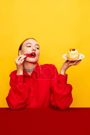 Foto de Extraordinary cake presentation. Beautiful young girl in red shirt over yellow studio background. Food pop art photography. Complementary colors. Concept of art, beauty, food. Copy space for ad, text. - Imagen libre de derechos