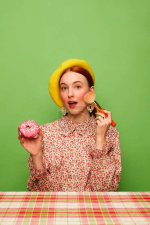 Téléchargez les photos : Cute looking. Beautiful girl with blushing cheeks eating pink donut over green background. Countryside style. Food pop art photography. Complementary colors. Concept of art, beauty. Copy space for ad - en image libre de droit