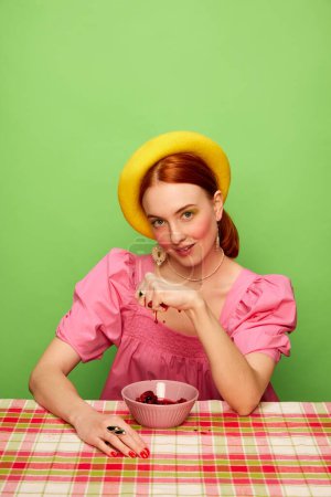 Foto de Estilo campestre. Hermosa joven en lindo vestido rosa comiendo mermelada de bayas sobre fondo verde. Fotografía de arte pop de comida. Colores complementarios. Concepto de arte, belleza, comida. Copiar espacio para anuncios, texto - Imagen libre de derechos