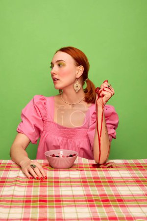 Photo for Countryside style. Beautiful young girl in cute pink dress eating berry jam over green background. Food pop art photography. Complementary colors. Concept of art, beauty, food. Copy space for ad, text - Royalty Free Image