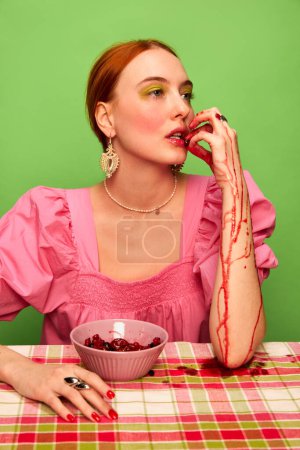 Téléchargez les photos : Style campagnard. Belle jeune fille en robe rose mignonne mangeant de la confiture de baies sur fond vert. Photographie pop art culinaire. Couleurs complémentaires. Concept d'art, de beauté, de nourriture. Espace de copie pour annonce, texte - en image libre de droit