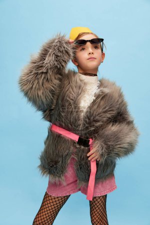 Photo for Extraordinary look. Beautiful little girl, child in trendy fur coat, paper crown and sunglasses posing over blue studio background. Concept of childhood, emotions, fun, lifestyle, facial expression - Royalty Free Image