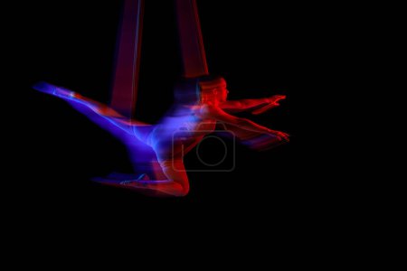 Foto de Flying. Young flexible girl doing aerial yoga, training over black studio background in neon with mixed lights. Concept of fitness, sportive lifestyle, health, strength, aerial yoga, anti-gravity yoga - Imagen libre de derechos