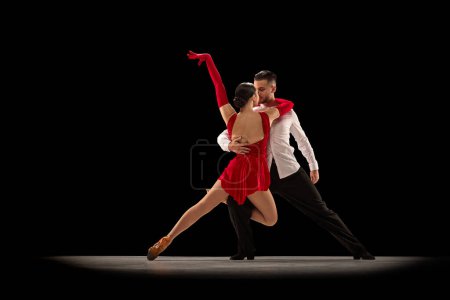 Téléchargez les photos : Passion and attraction. Young man and woman professional ballroom dancers dancing tango over black background. Concept of hobby, lifestyle, action, beauty of movements, emotions - en image libre de droit