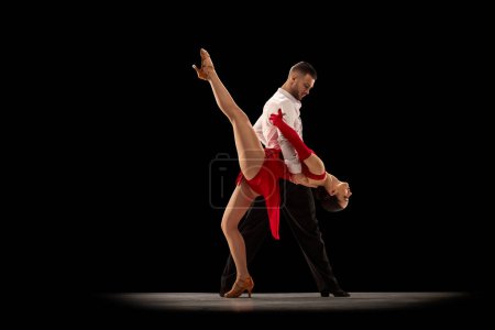 Foto de Young man and woman, professional talented dancers making classical performance, dancing tango, ballroom over black background. Concept of hobby, lifestyle, action, beauty of movements, emotions, art - Imagen libre de derechos