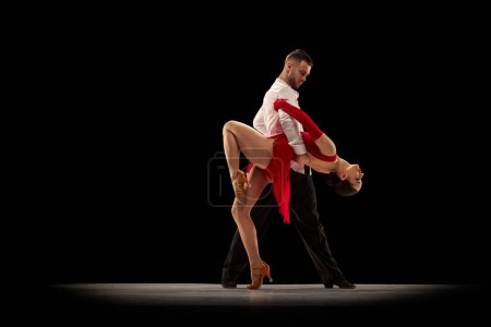 Photo for Passionate movements. Young handsome man and beautiful woman dancing tango, ballroom over black background. Concept of hobby, lifestyle, action, beauty of movements, emotions, fashion, art - Royalty Free Image