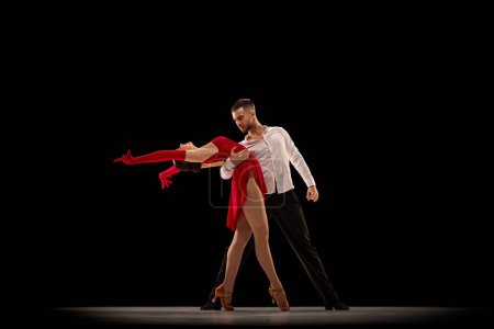 Foto de Hermoso, talentoso, atractivo joven y mujer, bailarines profesionales actuando, bailando tango sobre fondo negro. Concepto de estilo de vida, acción, belleza de movimientos, emociones, moda, arte - Imagen libre de derechos