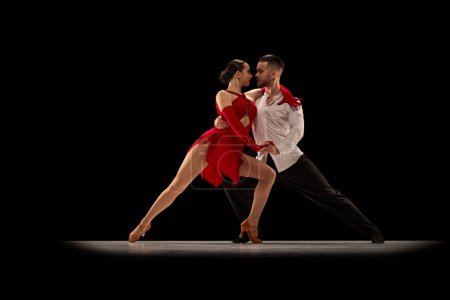 Téléchargez les photos : Beau, talentueux, attrayant jeune homme et femme, danseurs professionnels performant, tango dansant sur fond noir. Concept de style de vie, action, beauté des mouvements, émotions, mode, art - en image libre de droit