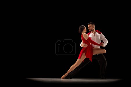 Foto de Talented performers. Beautiful young people, man and woman dancing tango over black studio background. Concept of hobby, lifestyle, action, beauty of movements, emotions, fashion, art - Imagen libre de derechos
