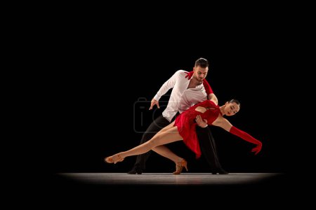 Foto de Beautiful, talented, attractive young man and woman, professional dancers performing, dancing tango over black background. Concept of lifestyle, action, beauty of movements, emotions, fashion, art - Imagen libre de derechos