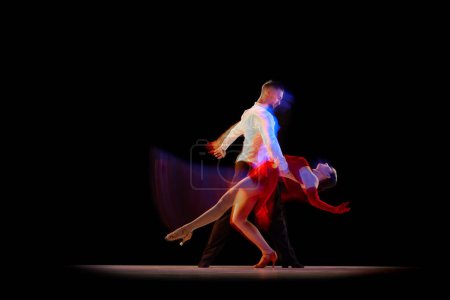 Foto de Hombre y mujer, bailarines profesionales realizando bailes de salón, tango sobre fondo negro con luces de neón mixtas. Concepto de hobby, estilo de vida, acción, belleza de movimientos, emociones, moda, arte - Imagen libre de derechos