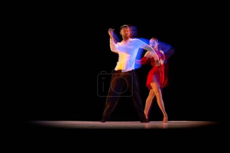 Foto de Movimientos dinámicos. Joven hombre y mujer bailando tango, salón de baile sobre fondo negro con luces de neón mixtas. Concepto de hobby, estilo de vida, acción, belleza de movimientos, emociones, moda, arte - Imagen libre de derechos