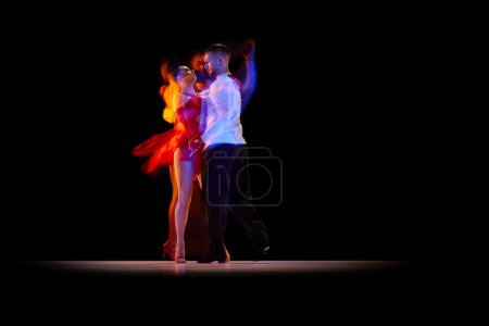 Téléchargez les photos : Beautiful young people, man and woman dancing tango, ballroom over black background with mixed neon lights. Concept of hobby, lifestyle, action, beauty of movements, emotions, fashion, art - en image libre de droit