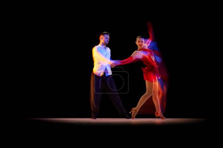 Photo for Expressive artistic young man and woman dancing tango, ballroom over black background with mixed neon lights. Concept of hobby, lifestyle, action, beauty of movements, emotions, fashion, art - Royalty Free Image