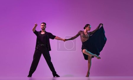 Téléchargez les photos : Man and woman, professional dancers in stylish, beautiful stage costumes performing tango on purple background on neon lights. Concept of lifestyle, action, beauty of movements, emotions, fashion, art - en image libre de droit