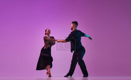 Foto de Man and woman, professional dancers in stylish stage costumes performing tango over purple background on neon lights. Concept of hobby, lifestyle, action, beauty of movements, emotions, fashion, art - Imagen libre de derechos