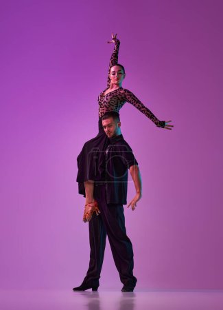Téléchargez les photos : Man and woman, professional tango, ballroom dancers in stylish, beautiful stage posing over purple background on neon lights. Concept of lifestyle, action, beauty of movements, emotions, fashion, art - en image libre de droit
