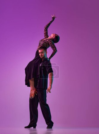 Foto de Hombre y mujer, tango profesional, bailarines de salón en un escenario elegante y hermoso posando sobre fondo púrpura sobre luces de neón. Concepto de estilo de vida, acción, belleza de movimientos, emociones, moda, arte - Imagen libre de derechos