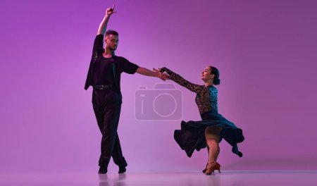 Foto de Joven y joven talentoso, bailarines profesionales realizando tango sobre fondo púrpura sobre luces de neón. Concepto de hobby, estilo de vida, acción, belleza de movimientos, emociones, moda, arte - Imagen libre de derechos