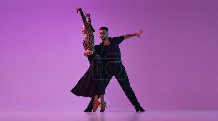 Foto de Young talented man and woman, professional dancers in stylish costumes performing tango on purple background on neon lights. Concept of , lifestyle, action, beauty of movements, emotions, fashion, art - Imagen libre de derechos